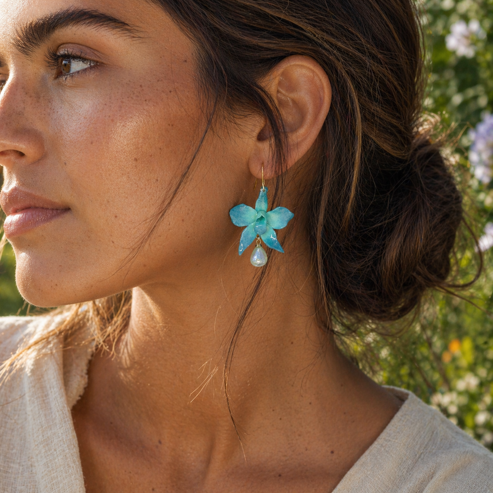 Close-up of a woman wearing turquoise orchid earrings with a blurred natural background