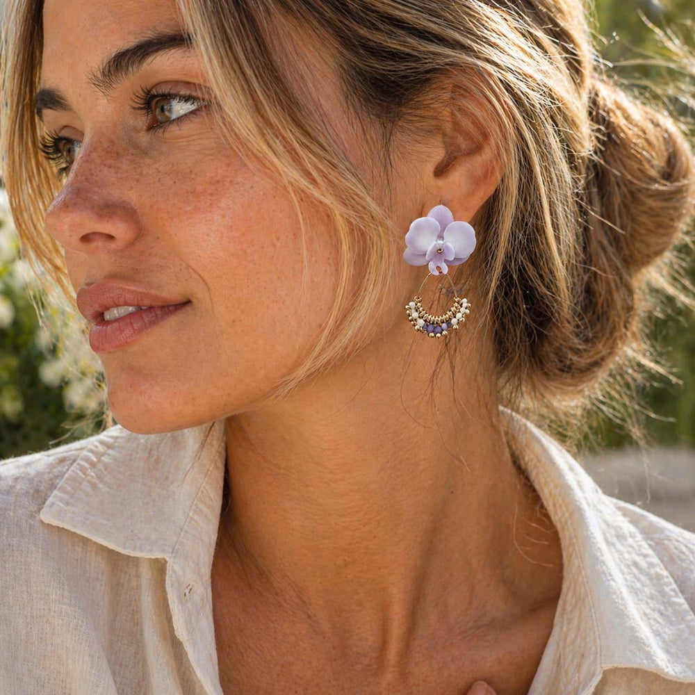 Woman wearing a purple orchid earring with a blurred natural background