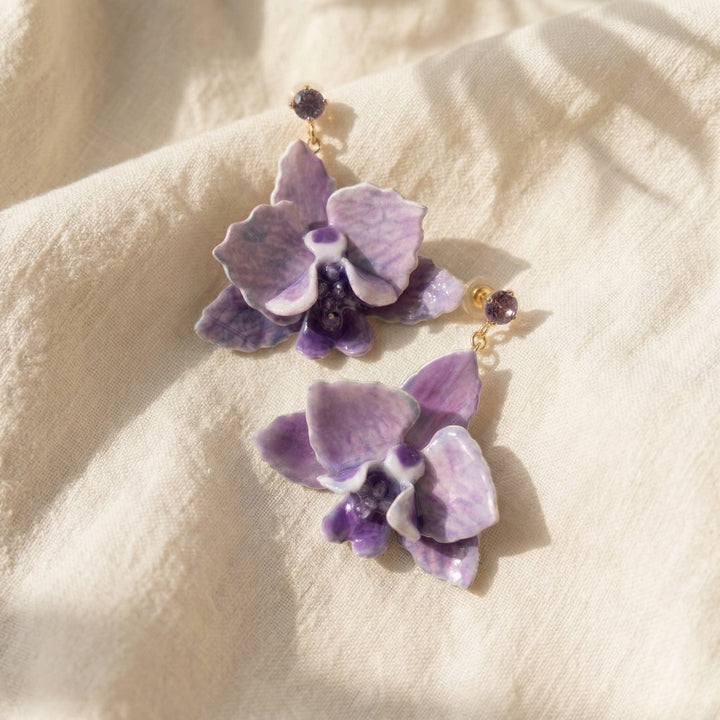 Purple floral earrings on a beige fabric background