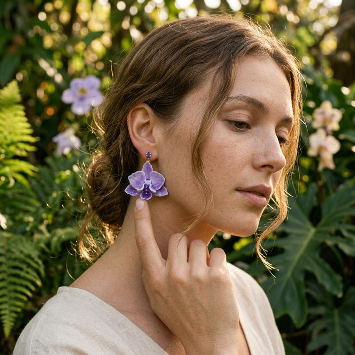 Woman wearing purple orchid earrings in a natural setting with greenery