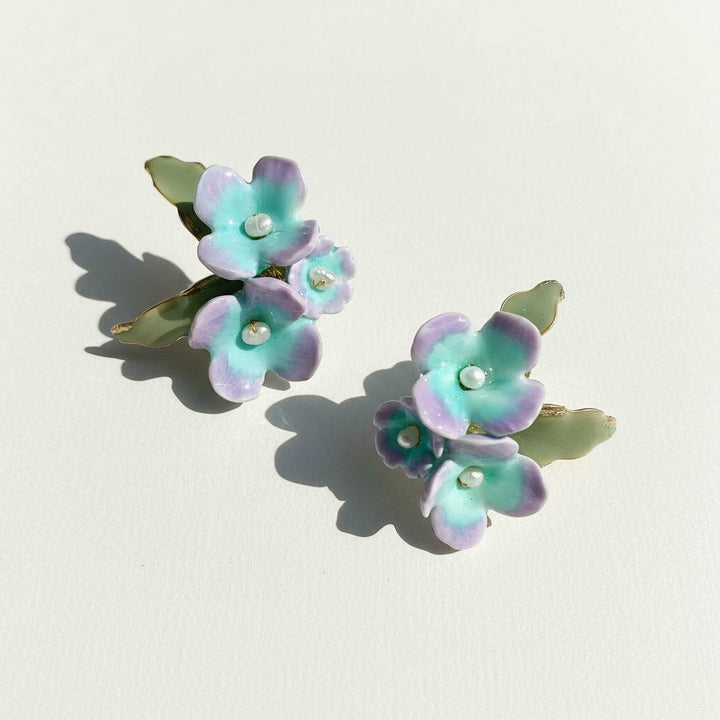 Pair of floral earrings with green leaves on a light background