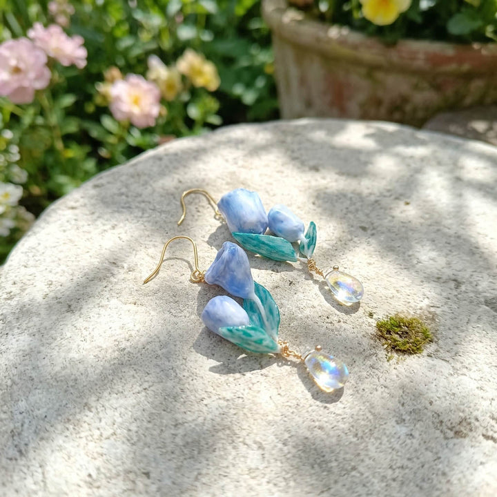 Blue and green floral earrings on a stone surface with flowers in the background