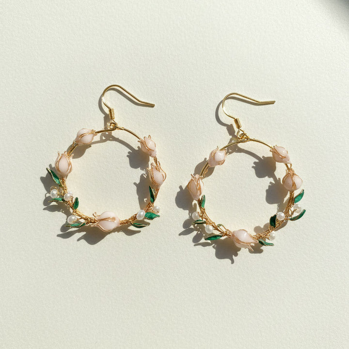 Gold hoop earrings with floral and pearl details on a light background
