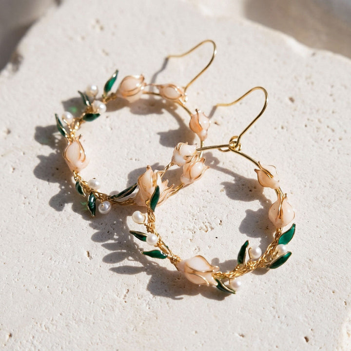 Gold hoop earrings with lily of the valley and pearl details on a light background