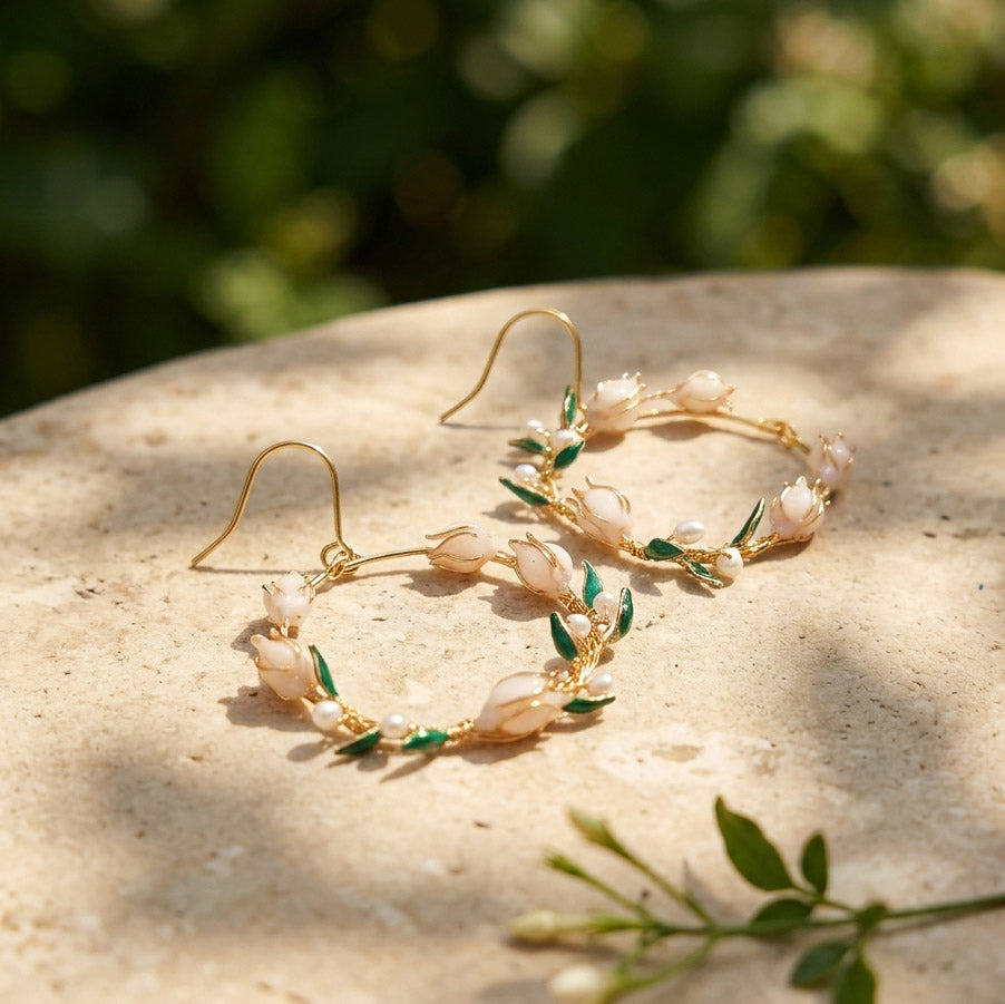 Gold earrings with lily of the valley design on a stone surface with greenery in the background