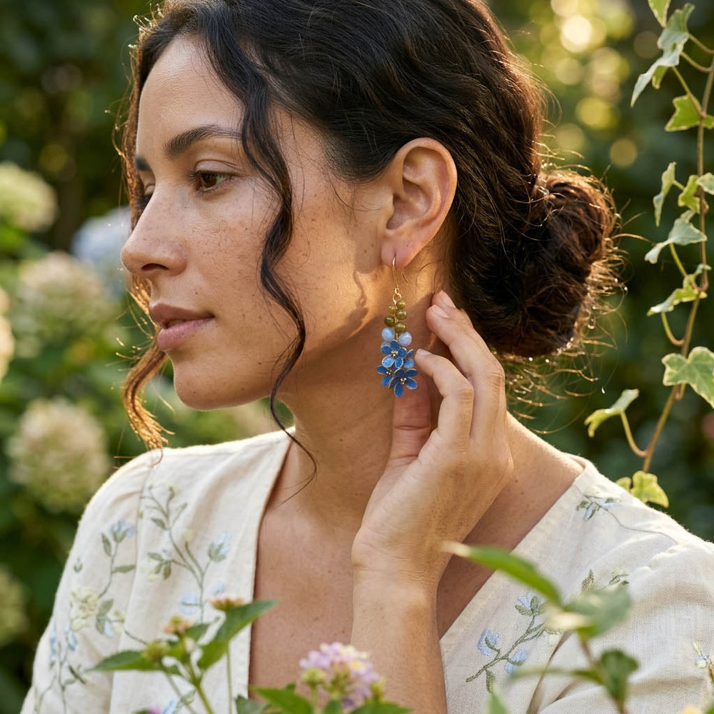 Woman wearing blue floral earrings outdoors with greenery in the background