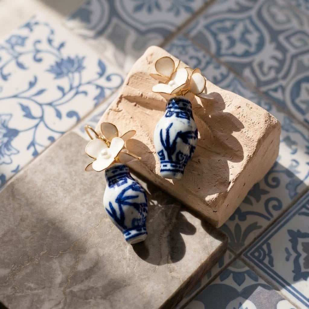 Pair of blue and white ceramic earrings with gold accents on a textured surface.