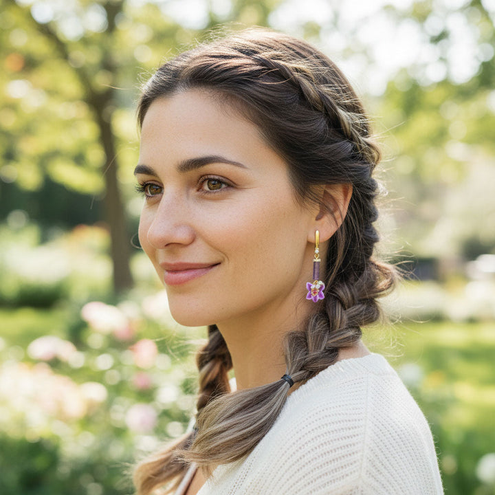 Woman with braided hair wearing purple orchid earring in a park setting