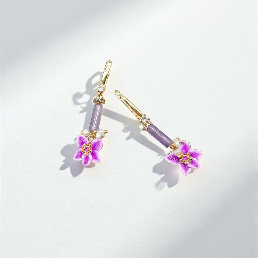 Pair of earrings with purple gemstones and floral designs on a light gray background