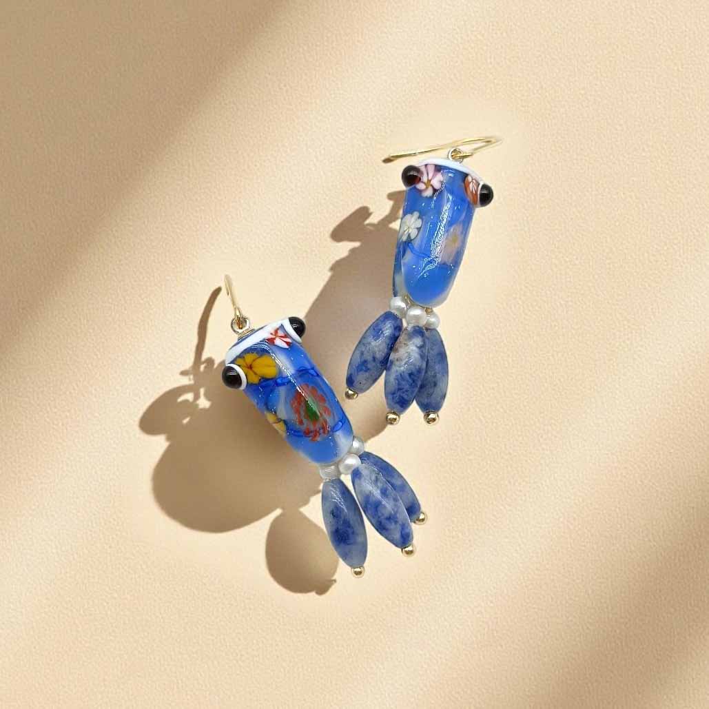 Blue glass earrings with floral designs on a beige background
