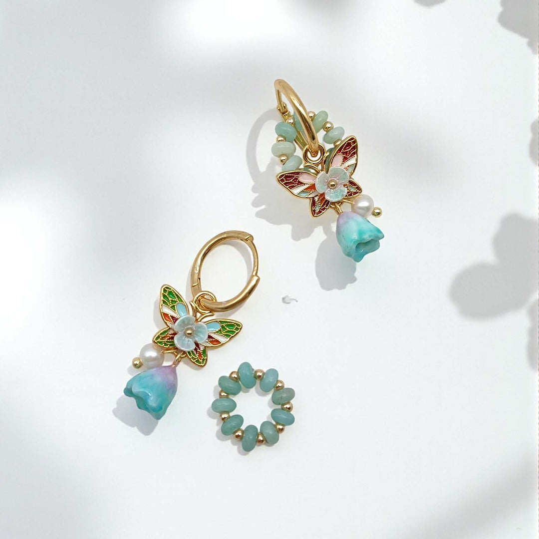 Pair of gold earrings with butterfly and floral designs on a light background