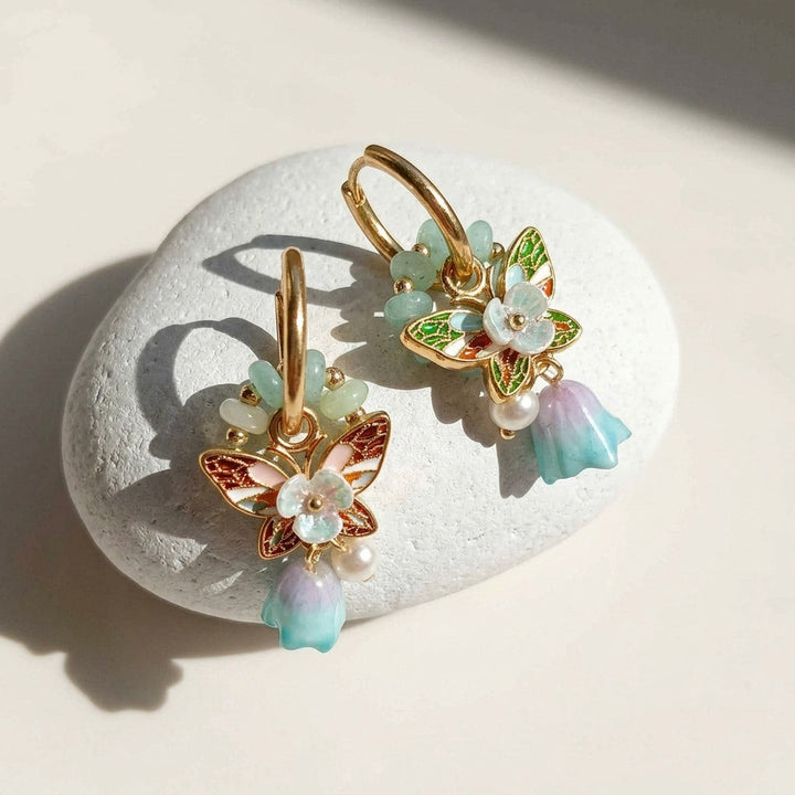 Butterfly-shaped earrings with floral details on a stone surface