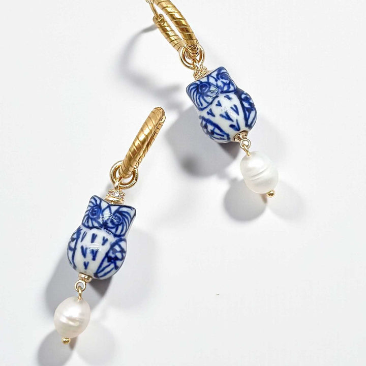 Pair of earrings with blue and white ceramic owl-shaped beads and gold accents on a light background