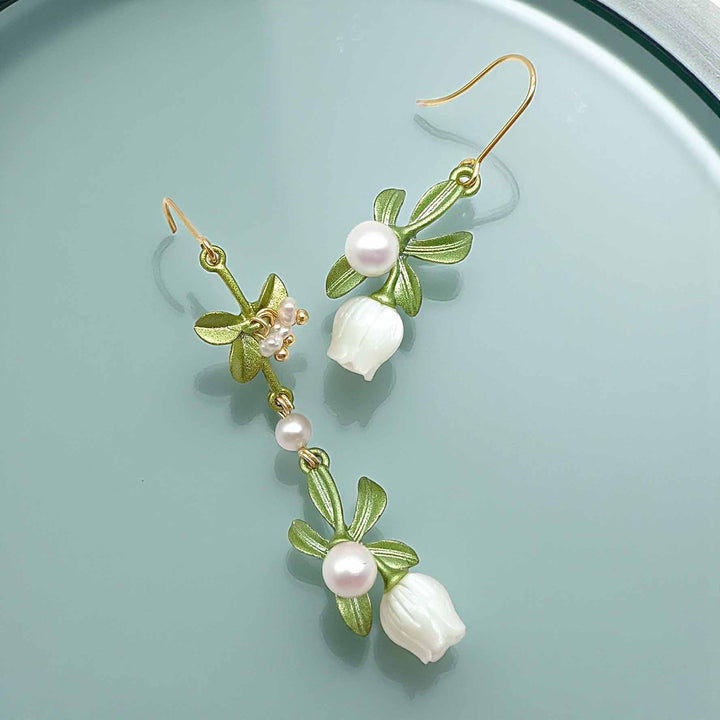 Floral earrings with green leaves and white flowers on a light blue background