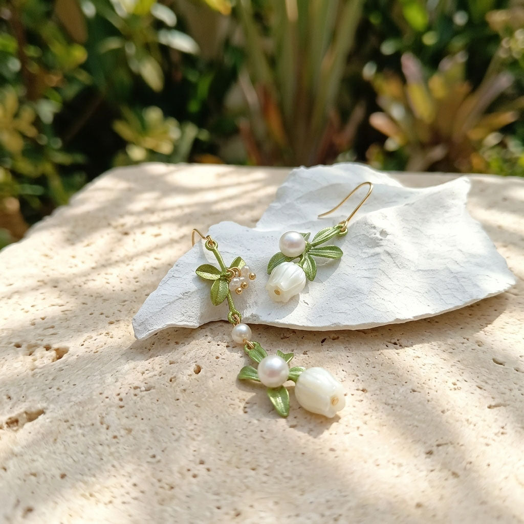 Pair of pearl earrings with green leaves on a white shell against a natural background