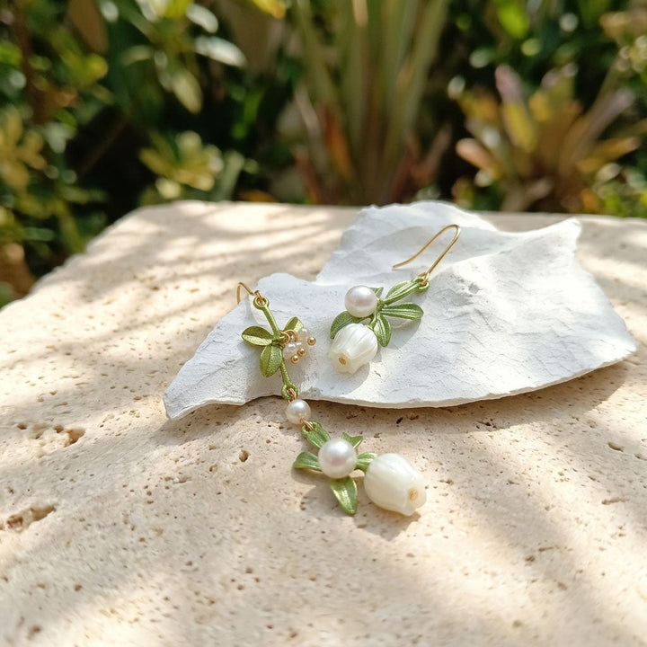Pair of pearl earrings with green leaves on a white shell against a natural background