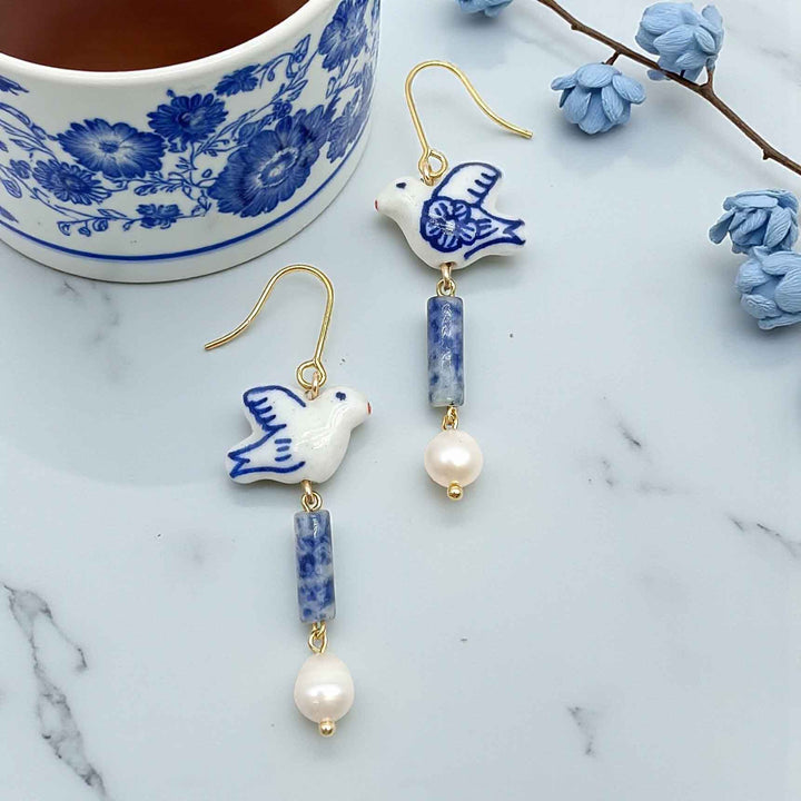 Ceramic dove earrings with blue and white design on a marble surface with a floral teacup.