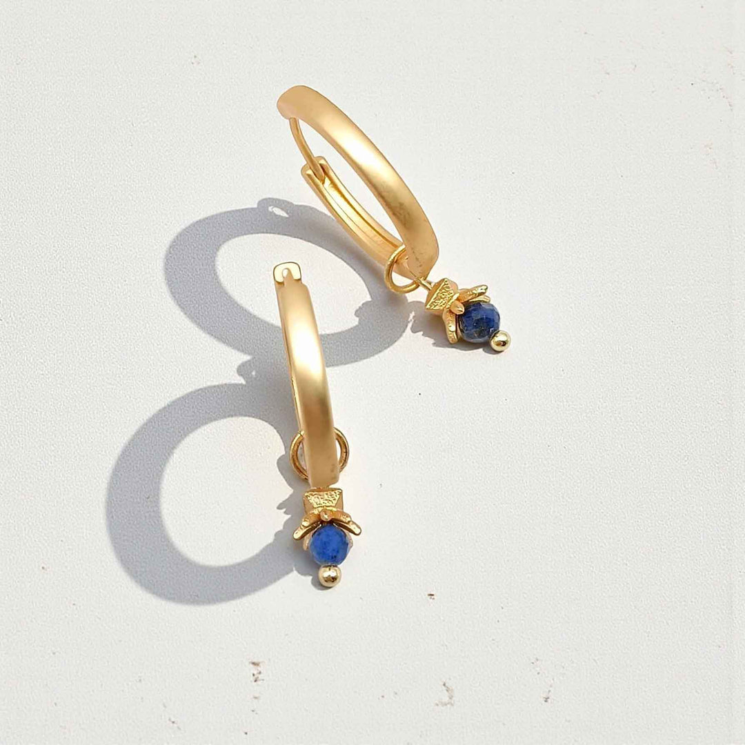 Gold hoop earrings with blue gemstones on a white background