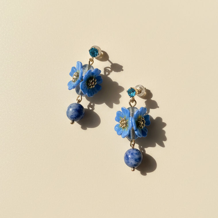 Handcrafted blue daisy flower earrings with lapis lazuli beads on neutral background.