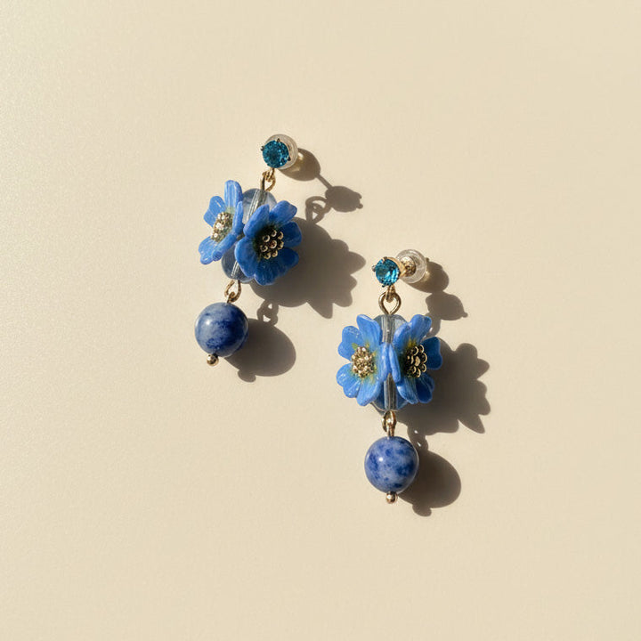 Handcrafted blue daisy flower earrings with lapis lazuli beads on neutral background.
