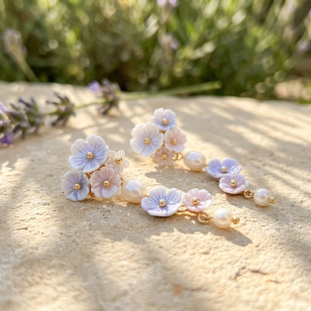 Floral earrings with pearls on a sandy surface with blurred lavender flowers in the background