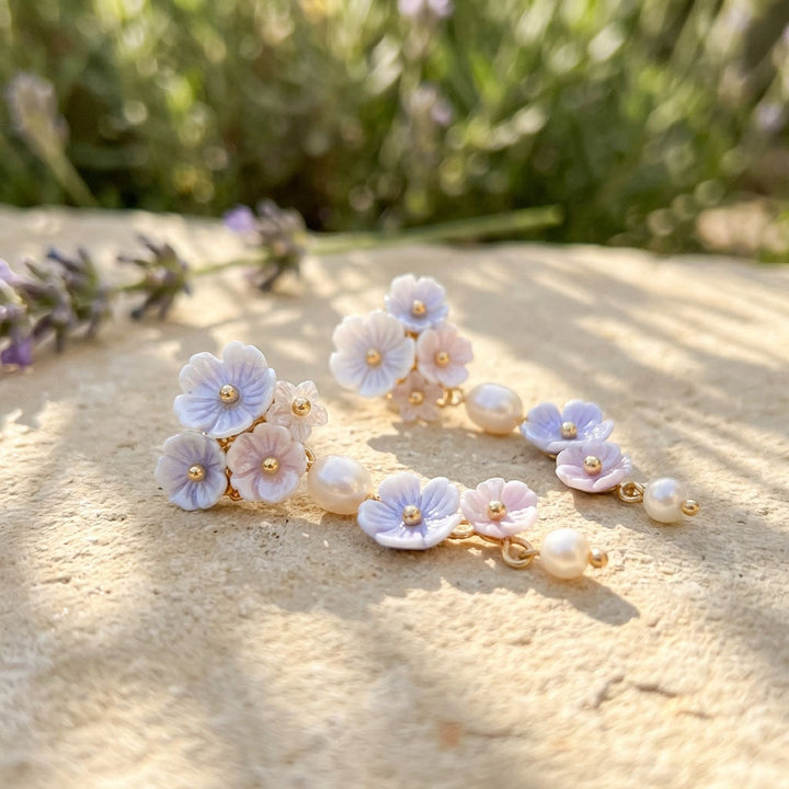 Floral earrings with pearls on a sandy surface with blurred lavender flowers in the background