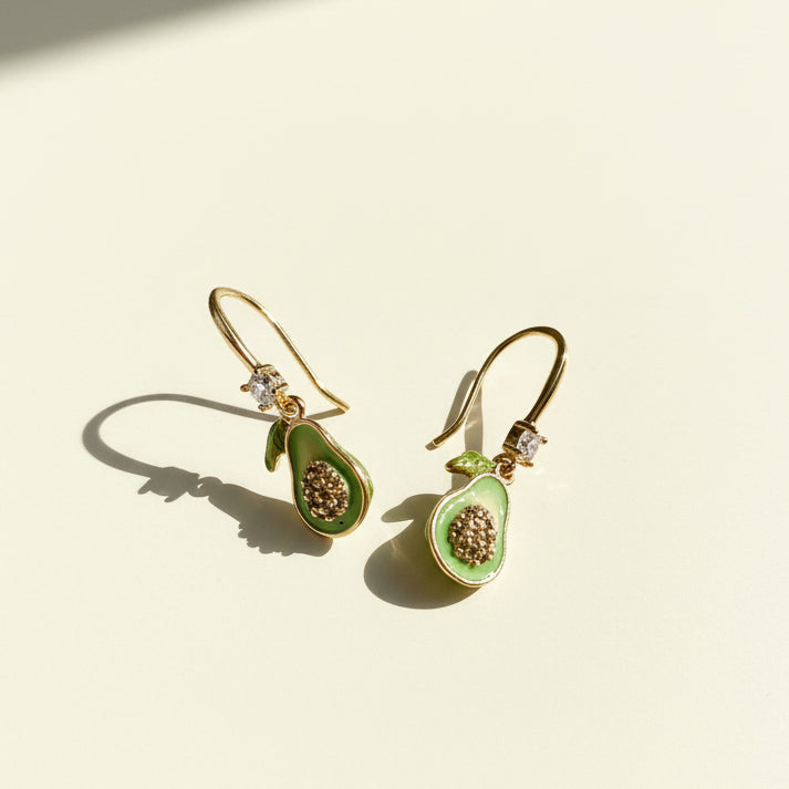 Hand-painted avocado hook earrings on cream background with sunlight and shadow.