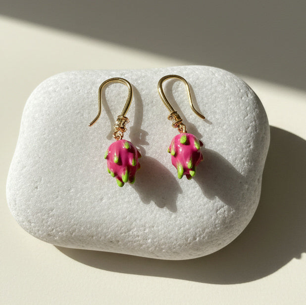 Close-up of enamel dragon fruit earrings with CZ stone on white stone background.