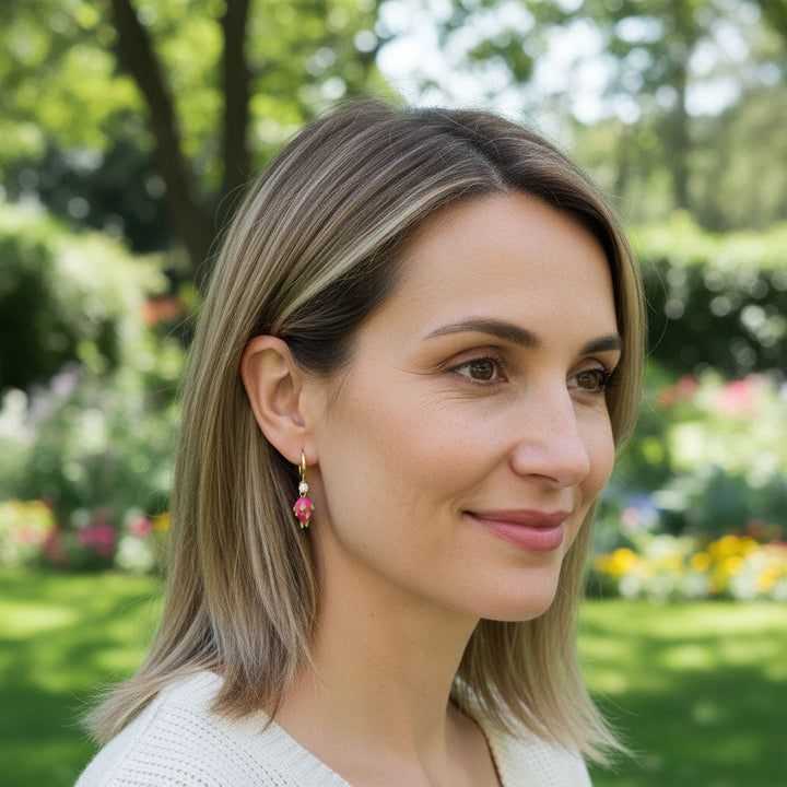 Model wearing A2K London pink dragon fruit enamel earrings in garden sunlight, tropical jewelry style.