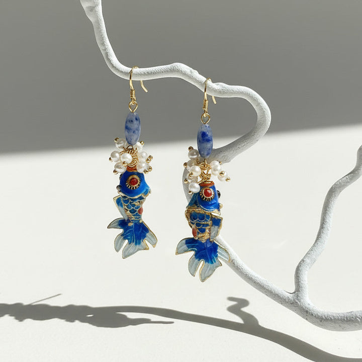 Close-up of koi fish cloisonné enamel earrings under sunlight.