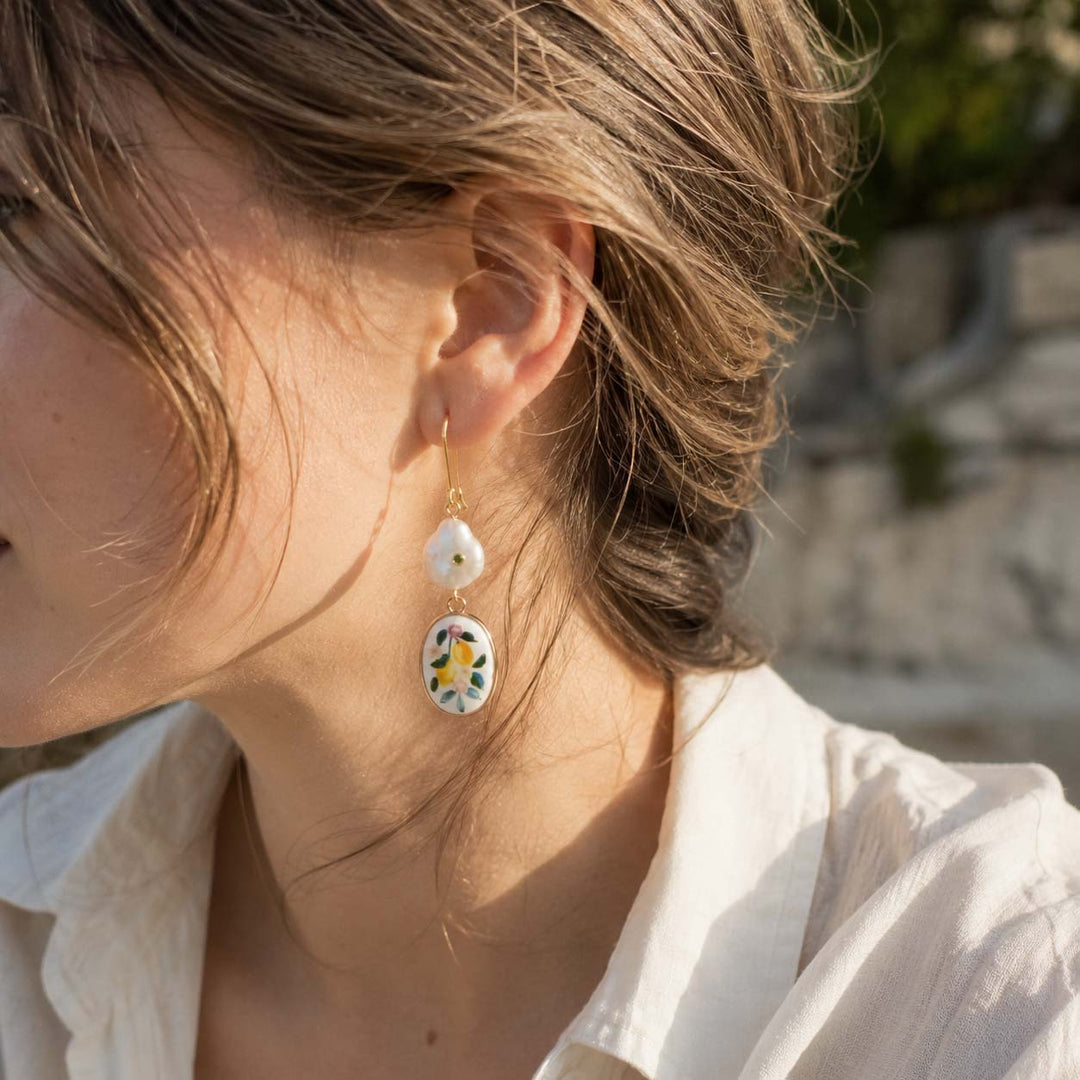 Close-up of a person wearing floral earrings with a blurred outdoor background