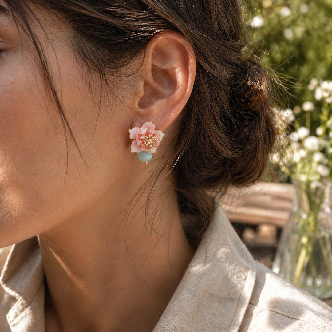 Close-up of a person wearing a peony earring with a blurred outdoor background