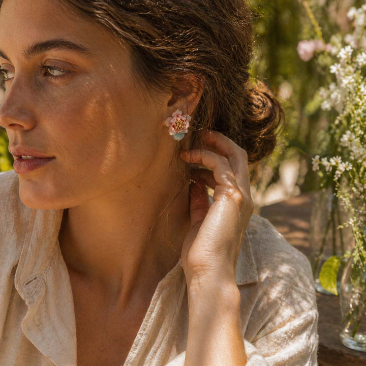 Woman adjusting her floral earring outdoors with flowers in the background