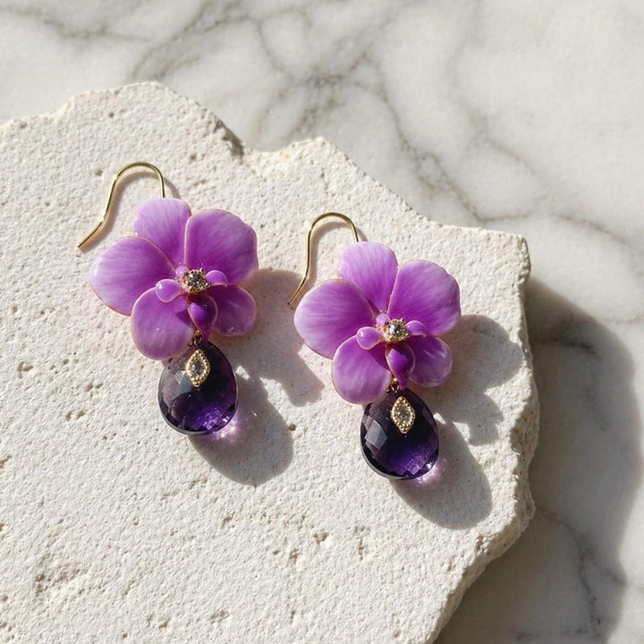 Purple orchid flower earrings with amethyst drops on a stone surface