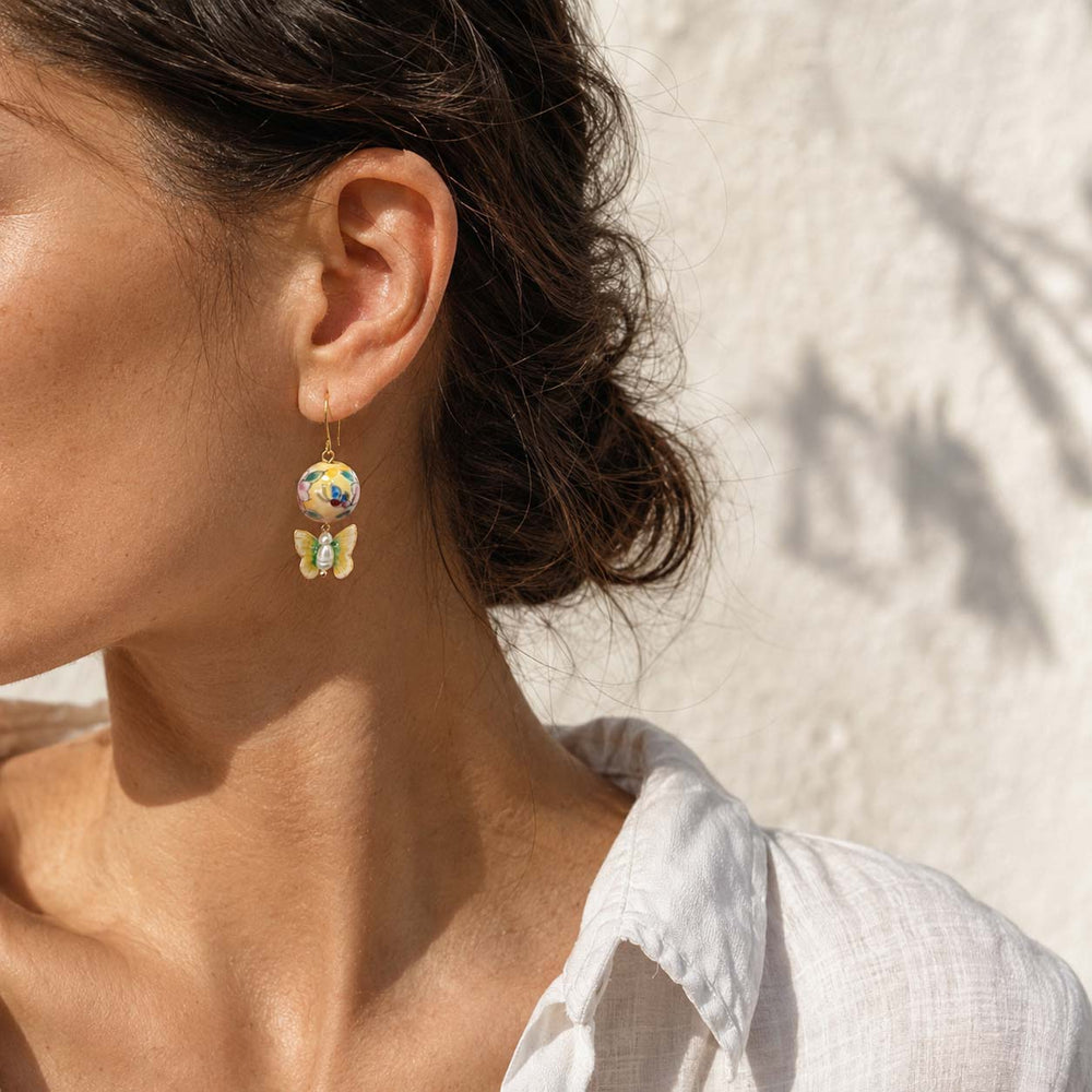 Close-up of a woman wearing hand-painted porcelain beads with butterfly earrings with a neutral background