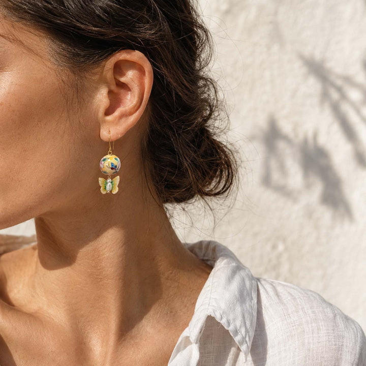 Close-up of a woman wearing hand-painted porcelain beads with butterfly earrings with a neutral background