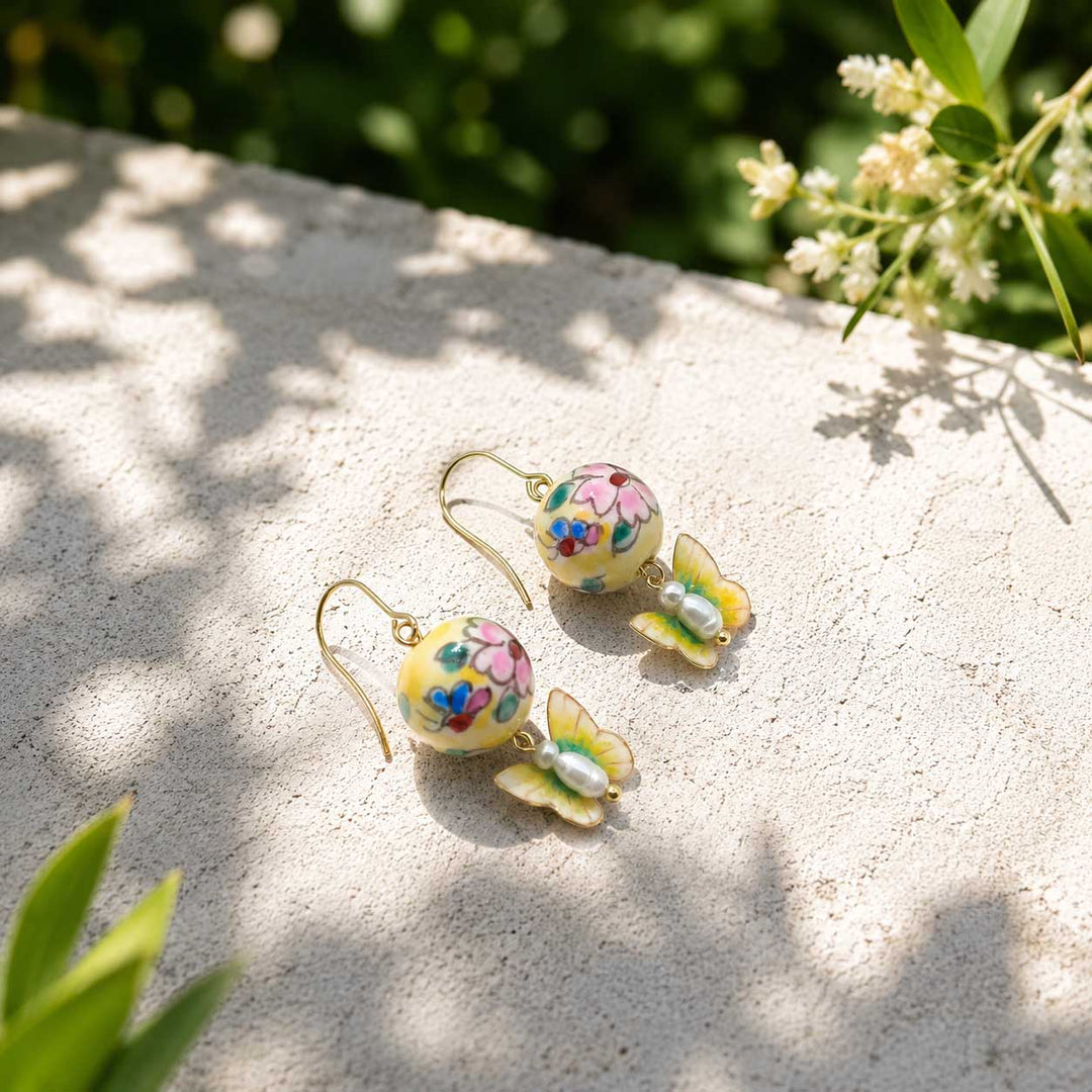 Nature-Inspired Butterfly Drop Earrings with Floral Porcelain Beads and Freshwater Pearls on a stone surface with greenery in the background