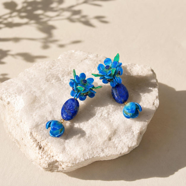Handcrafted forget me not flower drop earrings with lapis stone on textured white stone surface
