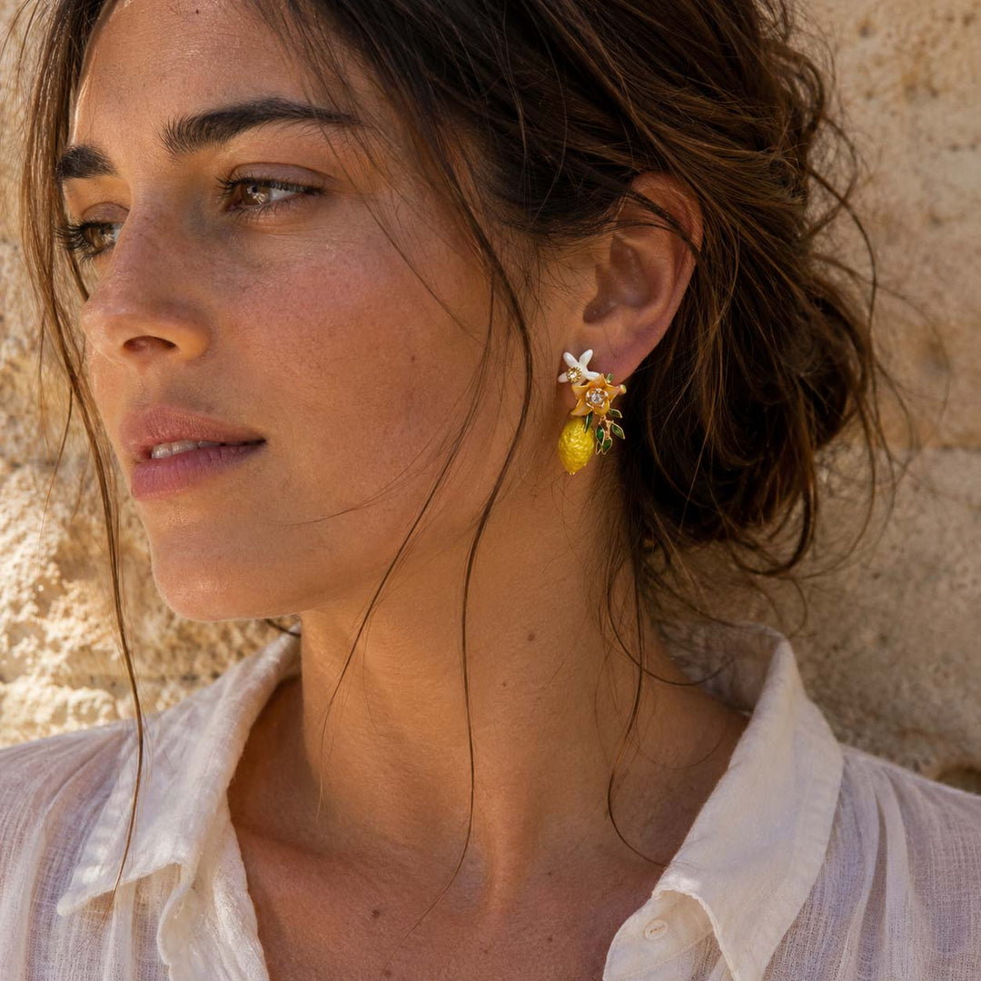 Woman wearing handcrafted lemon blossom stud earrings with hand-painted enamel flowers, resin blossoms and textured lemon charms.