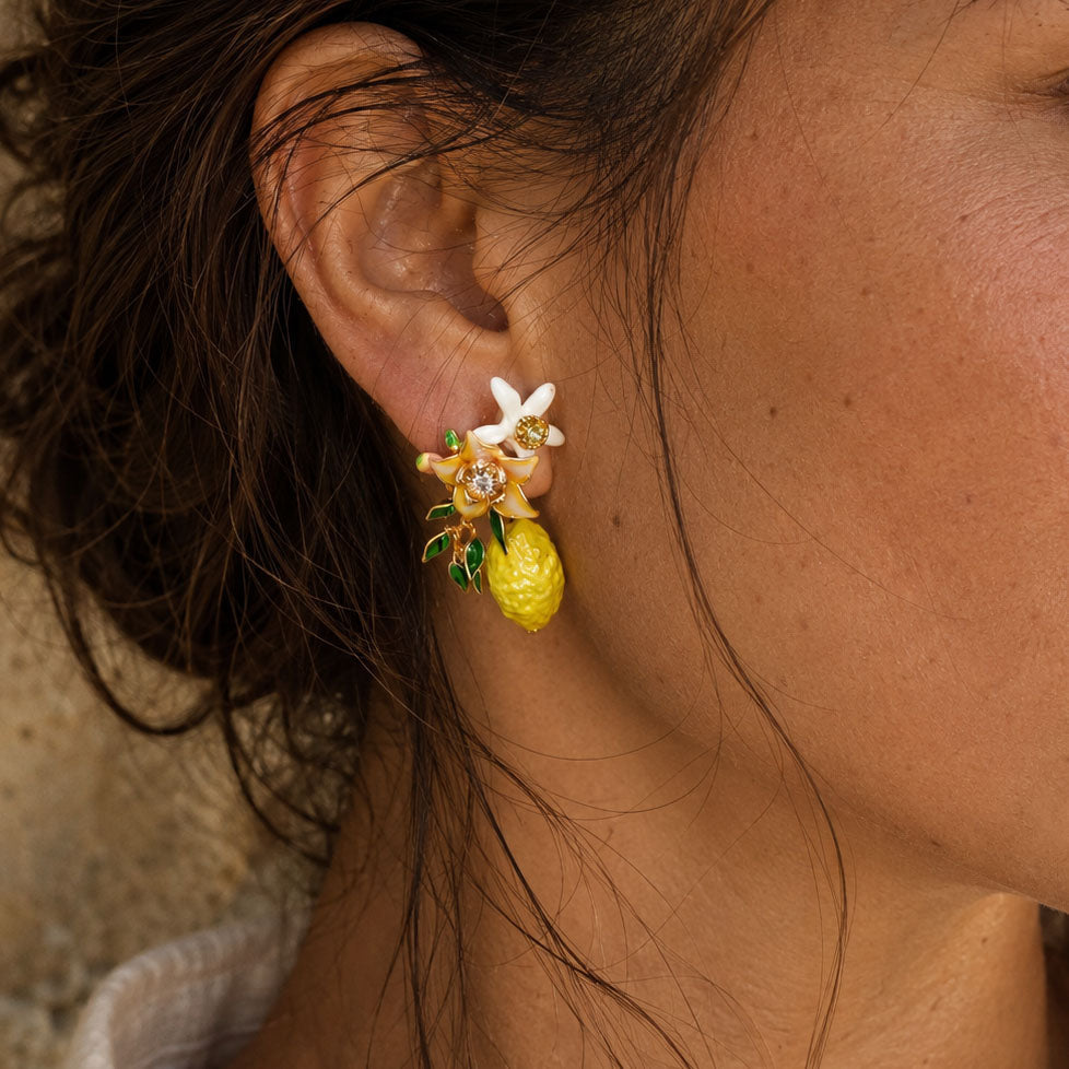 Close-up of hand-painted lemon blossom stud earrings featuring enamel flowers, handcrafted resin blossoms, green leaves and lemon charms.