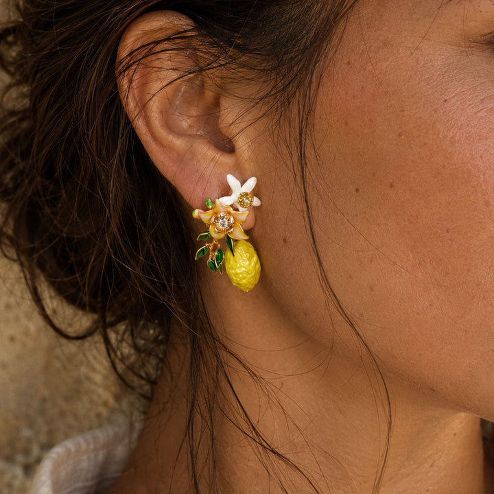 Close-up of hand-painted lemon blossom stud earrings featuring enamel flowers, handcrafted resin blossoms, green leaves and lemon charms.