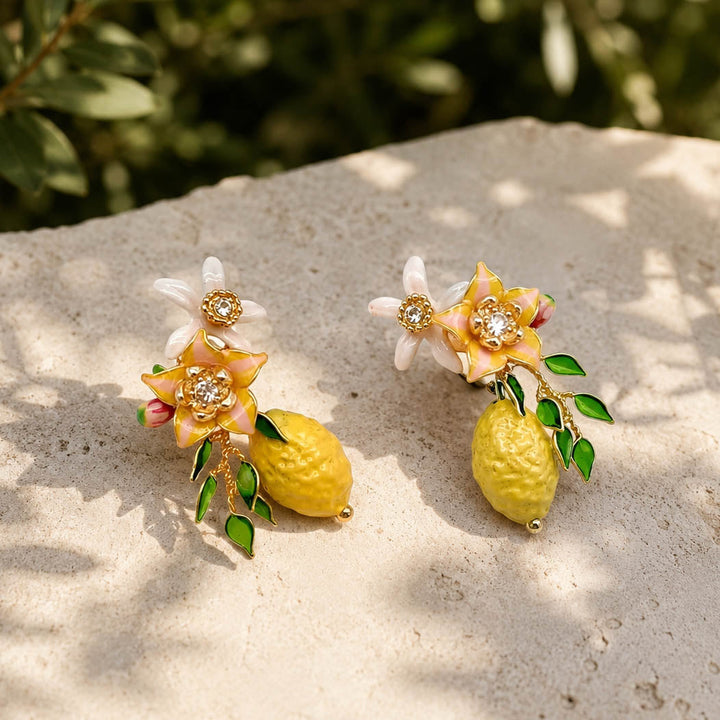 Handcrafted lemon blossom stud earrings styled on a natural stone surface in warm sunlight, featuring enamel flowers, resin blossoms and textured lemon charms.