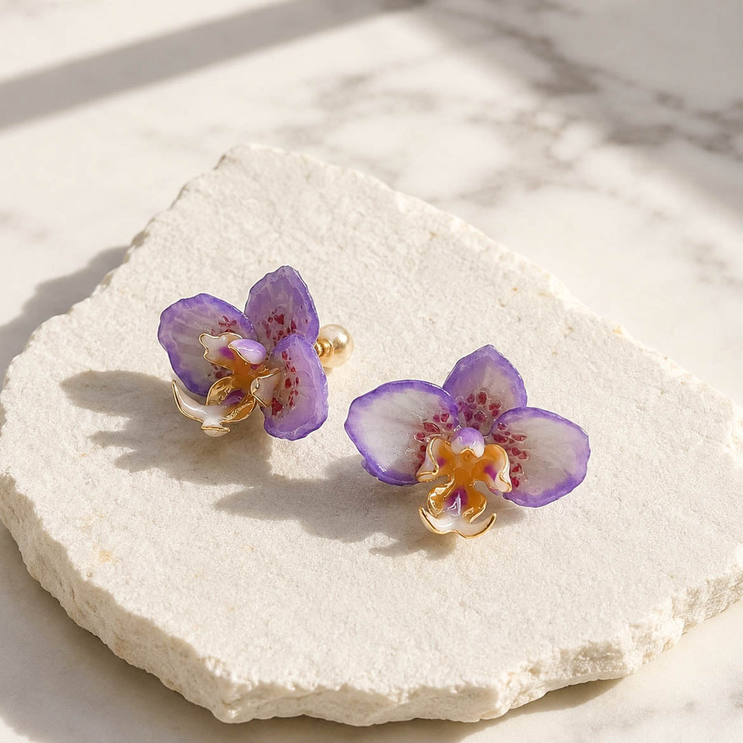Handpainted purple orchid flower stud earrings on textured white stone surface