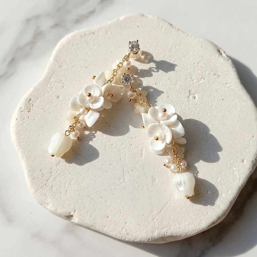 White floral drop earrings with handmade porcelain flowers, mother-of-pearl tulips and freshwater pearls on a sunlit stone surface.