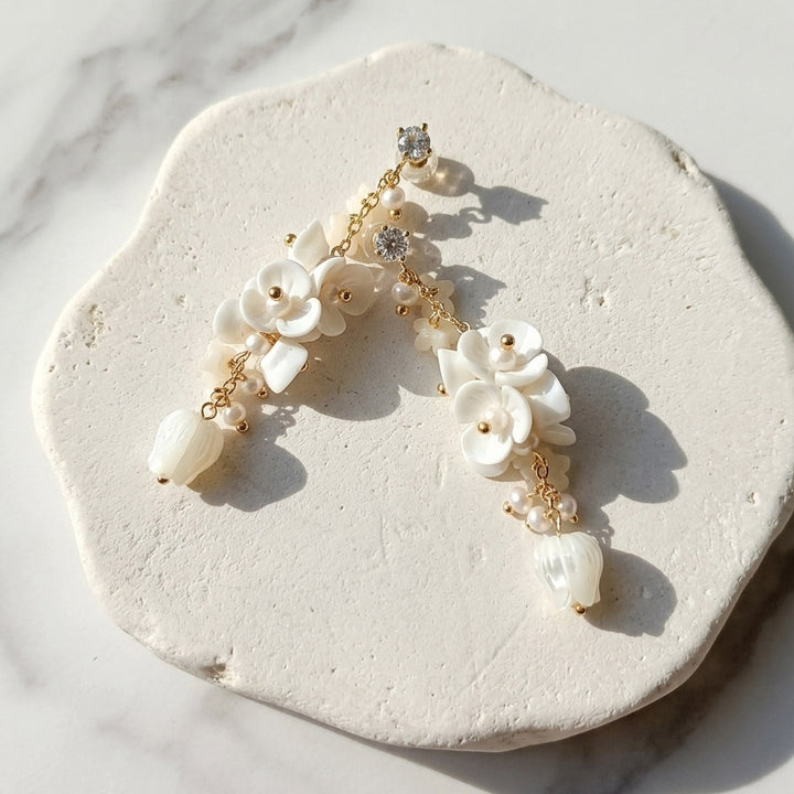 White floral drop earrings with handmade porcelain flowers, mother-of-pearl tulips and freshwater pearls on a sunlit stone surface.
