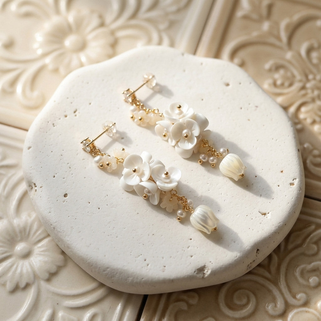 Porcelain flower and mother-of-pearl tulip drop earrings with CZ studs and freshwater pearls on pale textured stone.