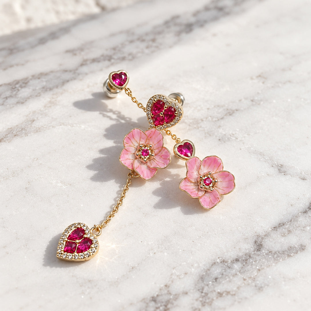 Pink sakura flower and heart CZ drop earrings arranged on a white marble surface in direct sunlight.