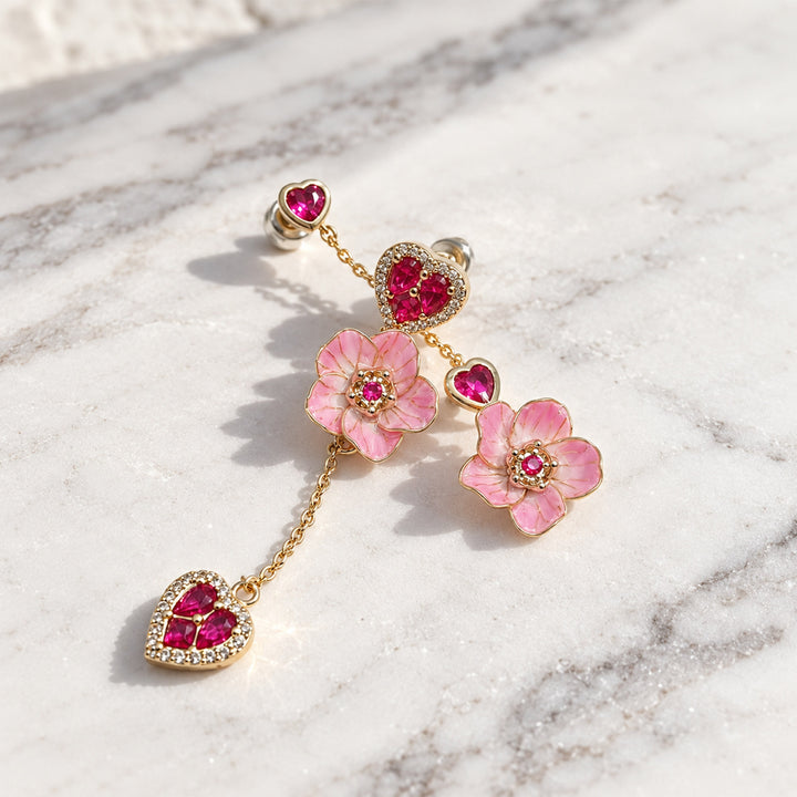 Pink sakura flower and heart CZ drop earrings arranged on a white marble surface in direct sunlight.