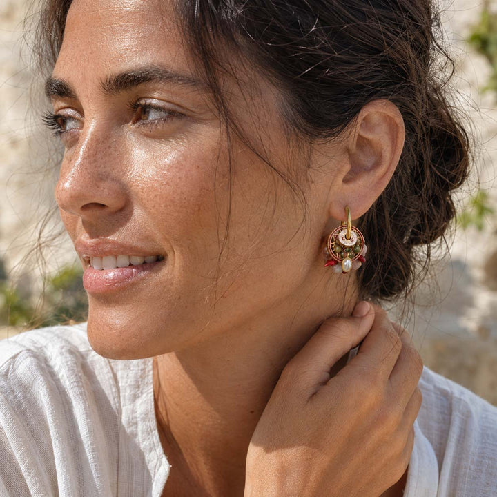 A close-up lifestyle shot of a woman wearing a pair of convertible earrings decorated with red and white enamel and rose quartz beads.