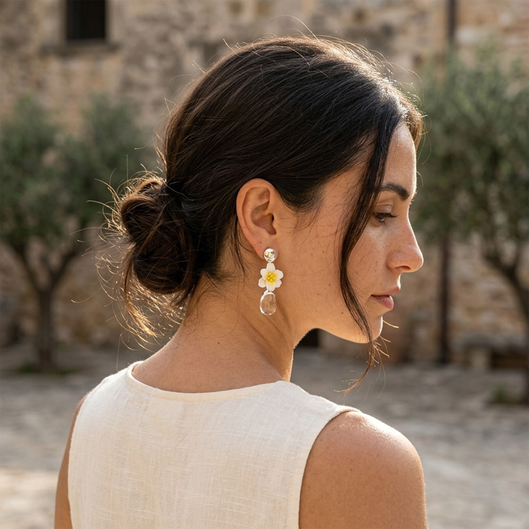 Model wearing jasmine flower and clear quartz drop earrings, photographed outdoors against a blurred stone building background.